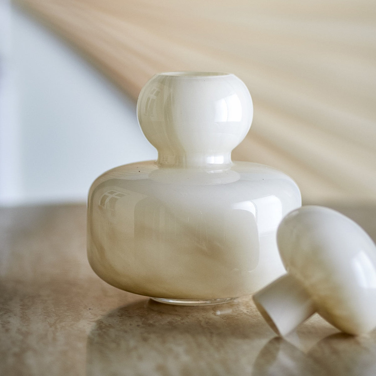 Cynthia Glass Vase 21cm in glossy beige, with a round body, ball-shaped neck and domed mushroom-style stopper, shown beside its lid on a marble surface.
