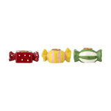 Set of three Leiano stoneware candle holders shaped like wrapped sweets with twisted ends, in red polka-dot, yellow-pink stripe, and green stripe designs with gold candle cups, on a white background.