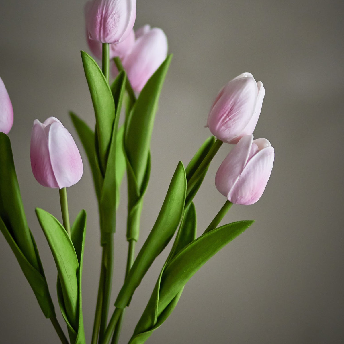 Tulip Artificial Bouquet in Pink, closed cupped blooms on long stems with slender green leaves, shown against a plain grey background.