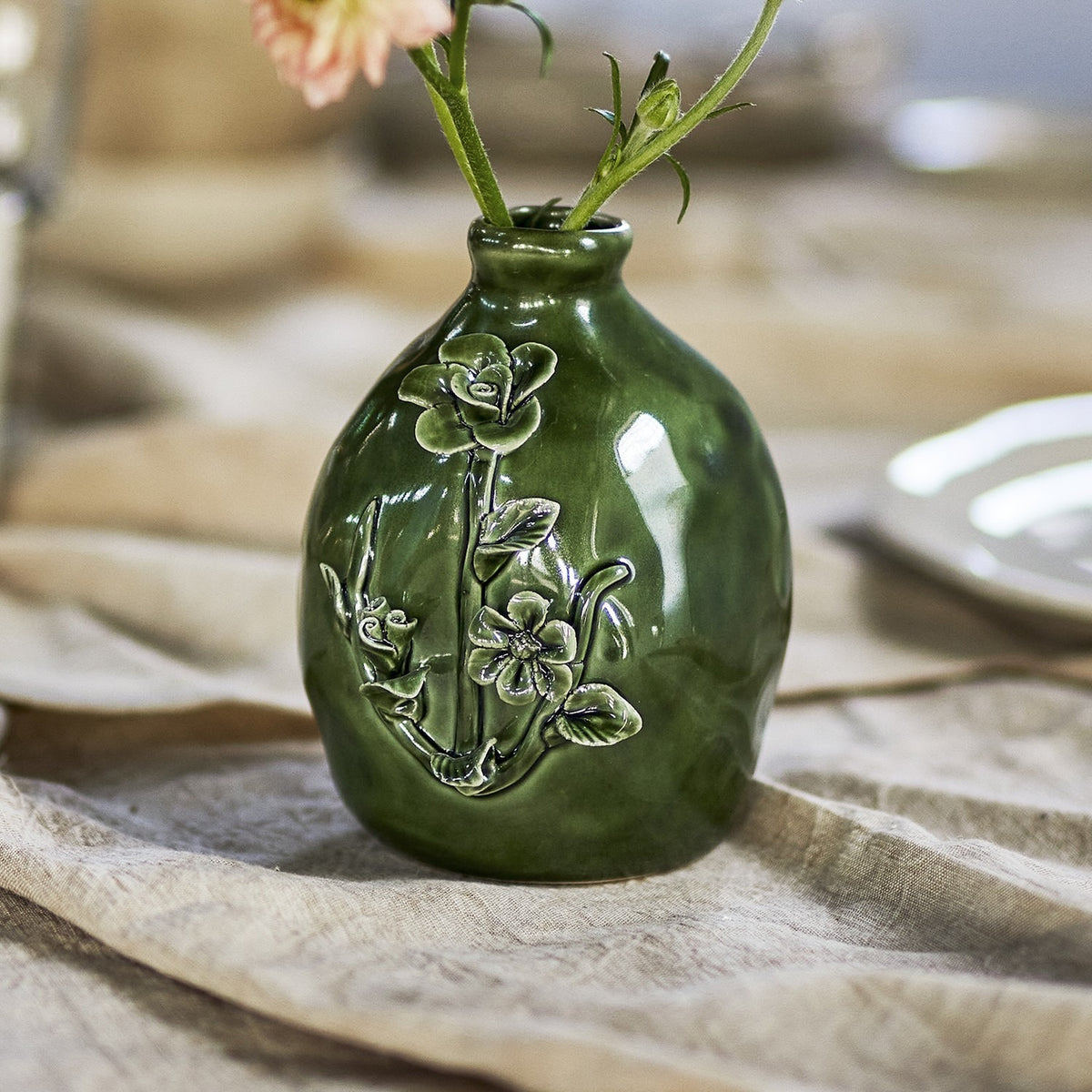 Ramia Floral Stoneware Vase in green, rounded ceramic body with raised floral relief design, holding a stem on a table setting.