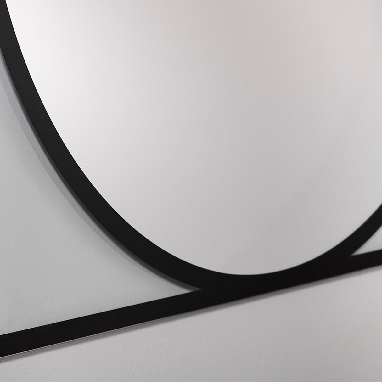 Close-up of the Circo square wall mirror's black frameless edge, showing a printed circular design in mirrored glass against a light grey wall.