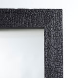 Close-up of the frame corner, the charred timber split into a tight crackled pattern where it meets the glass.