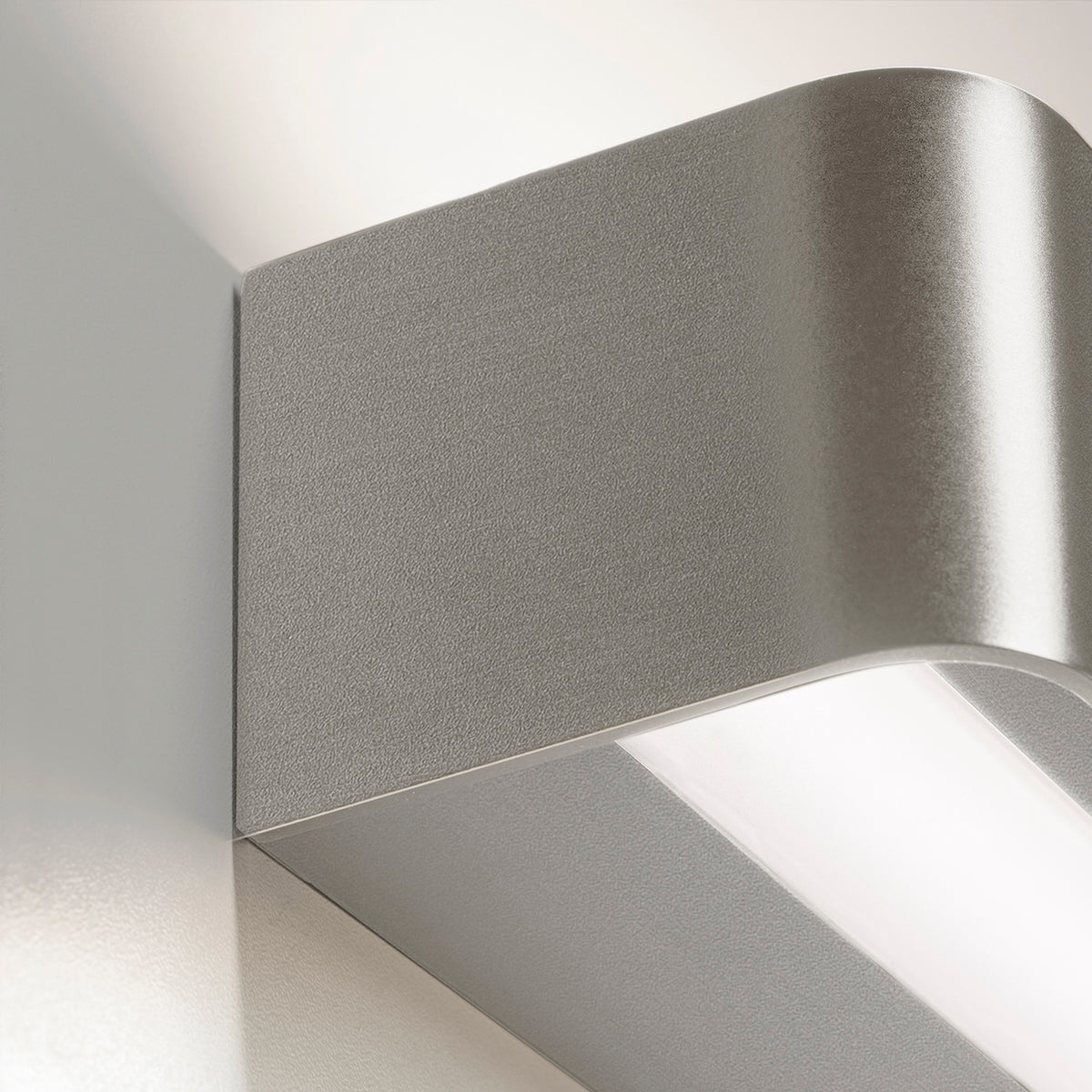Close-up of the Toy R LED Wall Light in brushed silver, showing its slim rectangular profile with a rounded edge and integrated LED strip casting upward and downward light.