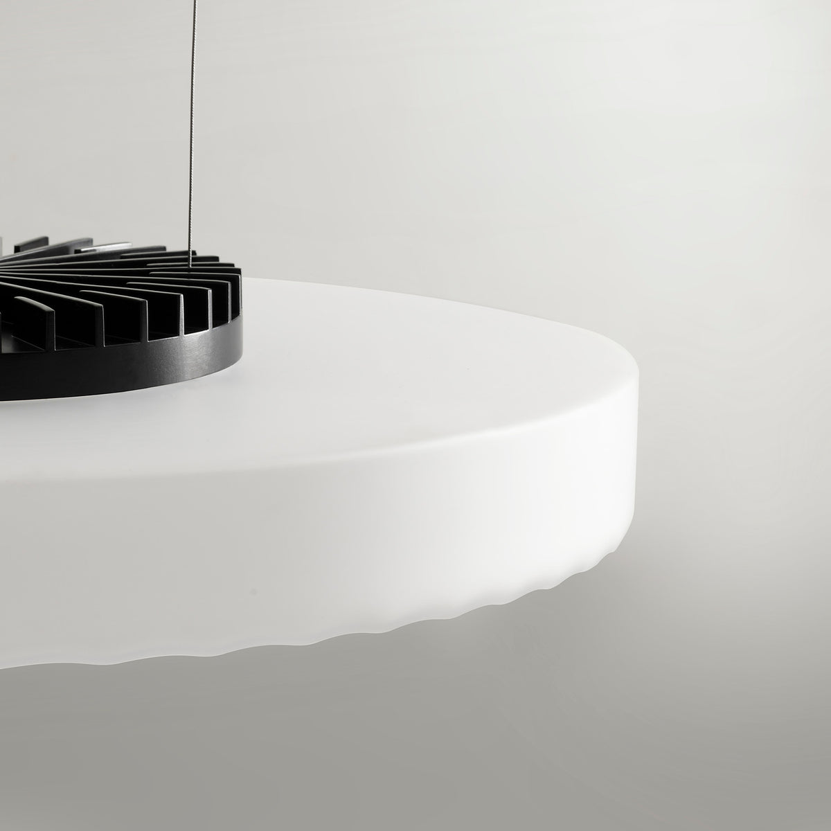 Close-up of the Côte pendant light's frosted white glass disc with ribbed underside, revealing the black integrated LED fixture above, set against a plain light background.