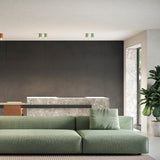 Paired green cylinder LED ceiling downlights, 10cm, mounted on a white ceiling above a dark-panelled living room with a green sofa.