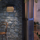 Sisal A/01 LED outdoor wall light with dark overhanging top and woven light beige fibre front, mounted on a stone wall illuminating an outdoor seating area at dusk.