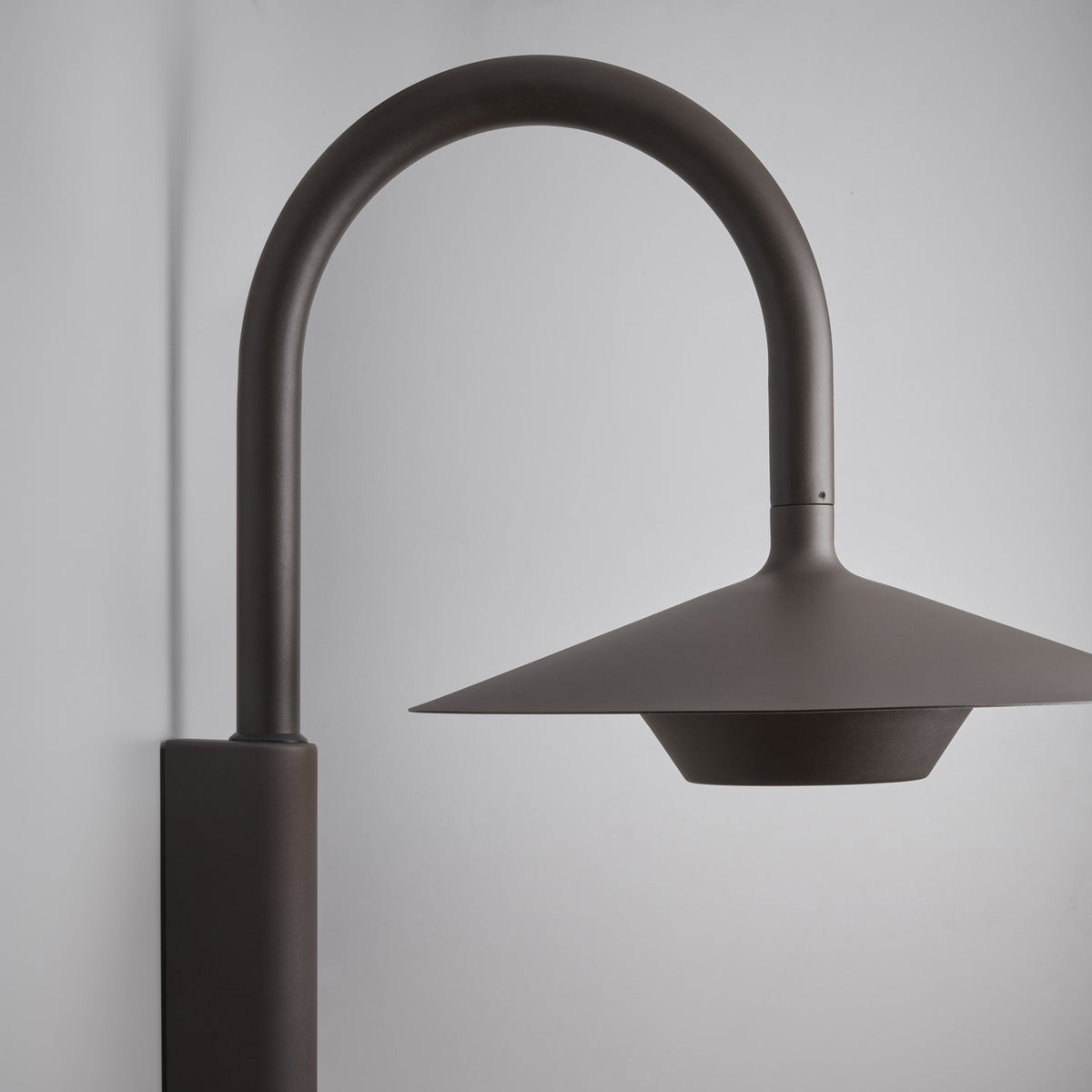 Fanalet A/02 outdoor wall light, close-up of the arched aluminium arm and wide flat shade in brown finish with white underside, shown against a plain grey background.