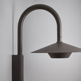 Fanalet A/02 outdoor wall light, close-up of the arched aluminium arm and wide flat shade in brown finish with white underside, shown against a plain grey background.