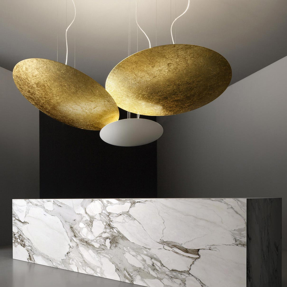 Gong Aluminium Disc LED Pendant Light 60cm, two large gold leaf discs and a white oval diffuser suspended above a marble reception counter in a grey interior.