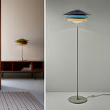 Overlay F Glass Tiered Floor Lamp with grey, blue and beige layered shades on a slim stem and round grey base, shown beside a matching table lamp in a living room setting.