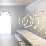Zero Round Vertical Ring Pendant Light, 98cm circular LED rings in brass finish, shown clustered over a dining table in a modern room with an arched doorway.