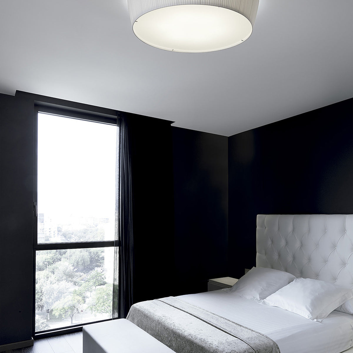 Plafonet 60 Ribbon LED ceiling light with pleated white drum shade mounted flush on a bedroom ceiling above a white tufted headboard and dark walls.