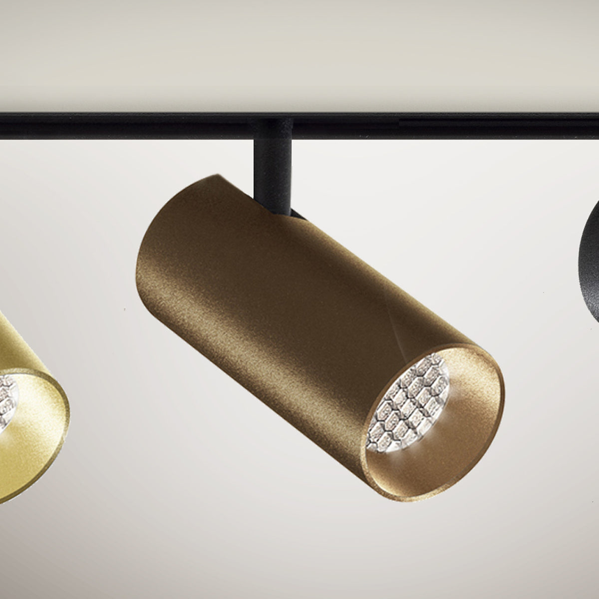 Street 8 Aluminium LED track spotlight with a slim cylindrical head in brushed bronze, mounted on a black stem from a track, shown beside gold and black finishes.