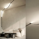 Matt Black Bow Wall 300 lighting accessory, a slim curved line with two fixing boxes, mounted along a ceiling and wall above a sofa, with a close-up of the illuminated curve against a plain wall.