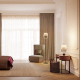 Adamas Smoke Grey Glass LED Floor Lamp with slim black stem and round base, faceted honeycomb shade, shown beside an armchair in a living room setting.