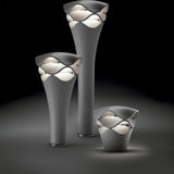 Cornet B/77 tiered LED bollard lights in stone grey, shown in three heights with wavy-layered heads glowing warm white, set against a dark background.
