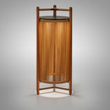 Kando P/111/R rechargeable outdoor floor lamp with teak wood frame, sand nautical cord cylinder shade glowing warmly, brown top disc and three-legged base, on a plain grey background.