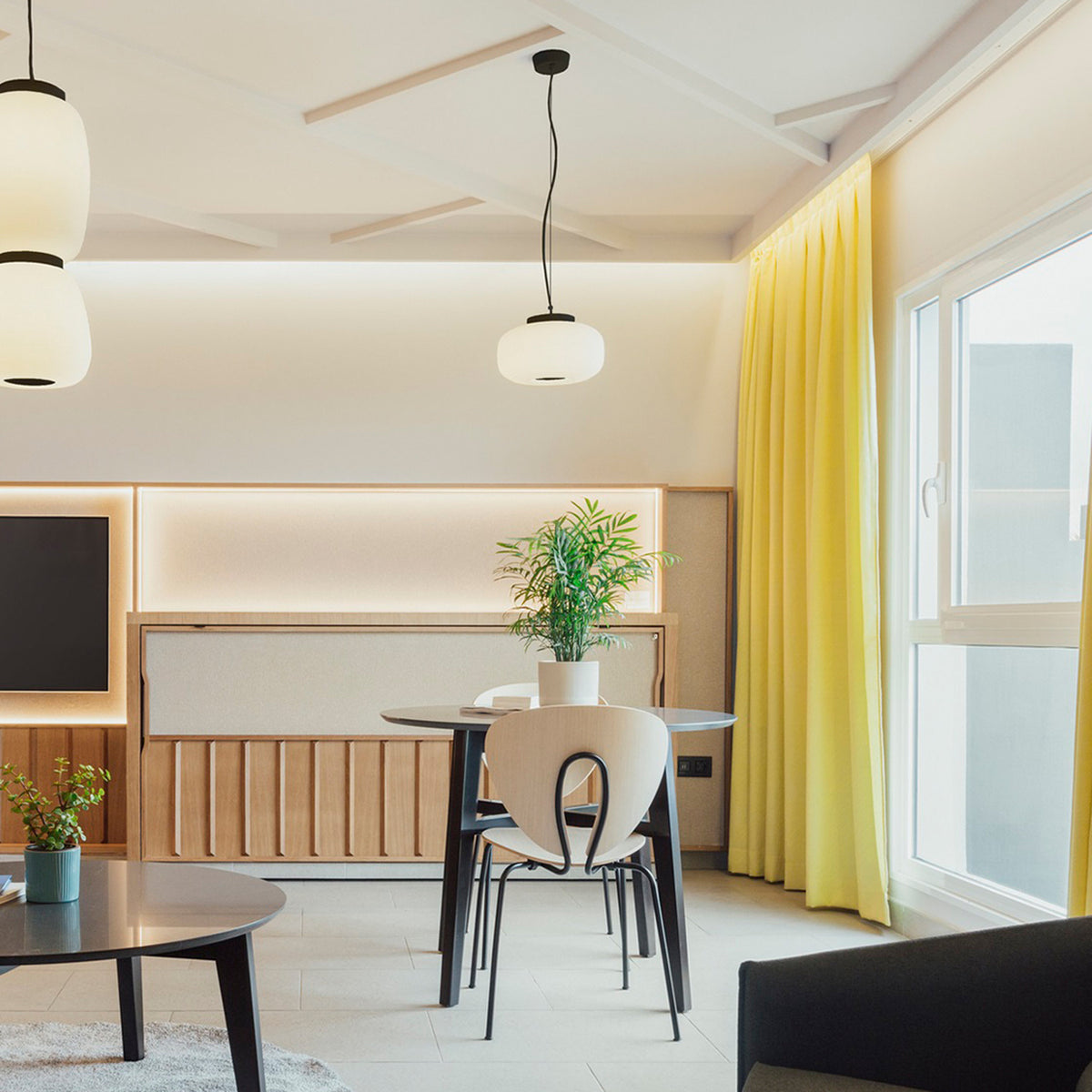 Misko S25 Glass Drum Pendant Light with a ribbed white glass shade and black collar on a cable, hanging above a dining table in a living space.