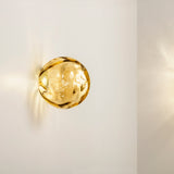 Murané Glass Sphere Wall & Ceiling Light, 15cm amber glass globe with rippled texture on a Brushed Champagne mount, mounted on a plain white wall and glowing warm white.