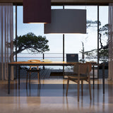 Noren S/151.2 dark grey fabric LED pendant light with curved rectangular shade, hung above a wooden dining table in a living space with large glass doors.