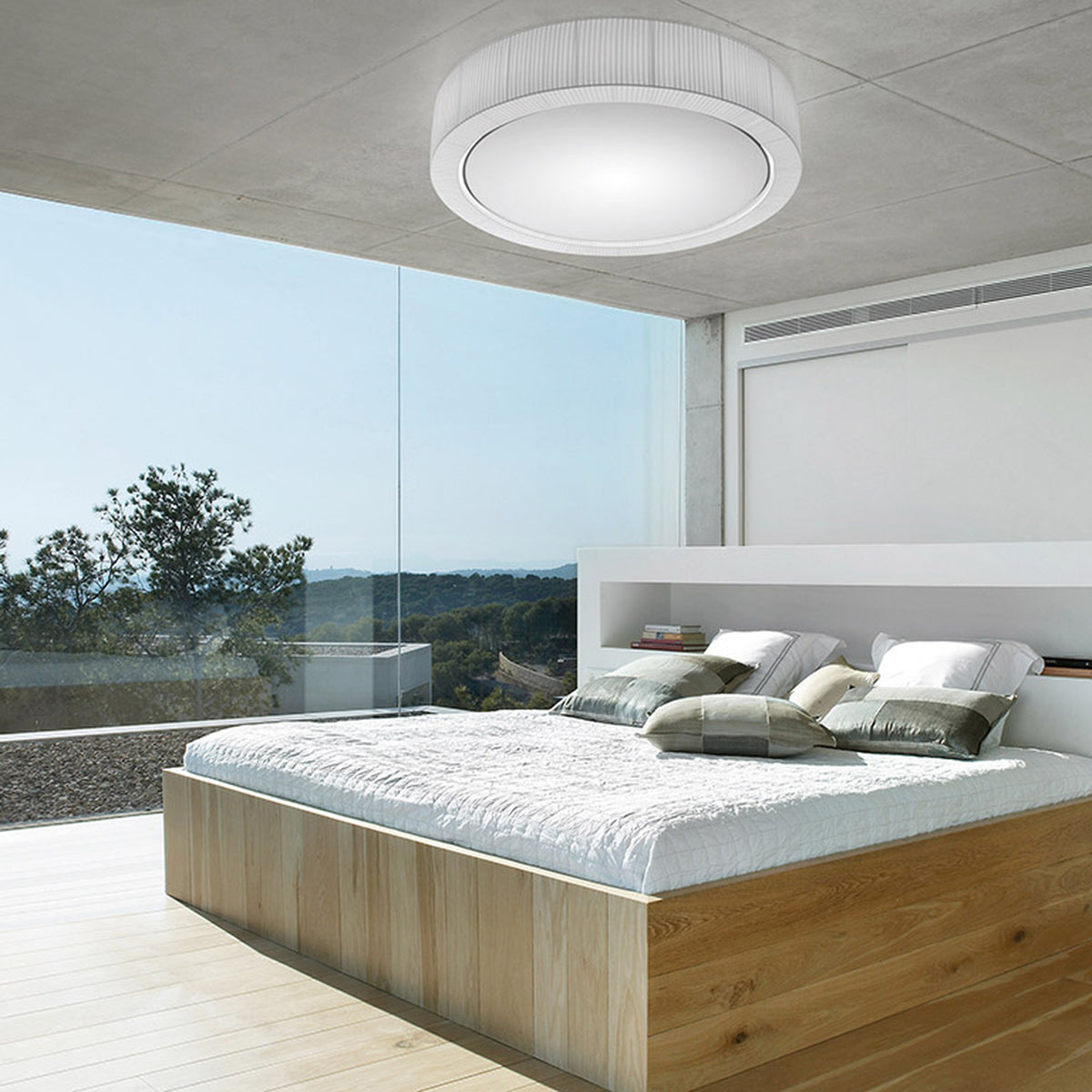 Urban PF/90 Ribbon LED ceiling light in white, round pleated drum with diffuser, mounted above a bed in a modern bedroom with floor-to-ceiling windows.