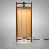 Kando P/111 Ribbon LED floor lamp with a tall pleated white cylinder shade inside a wood three-legged frame and dark top disc, lit against a plain light grey background.