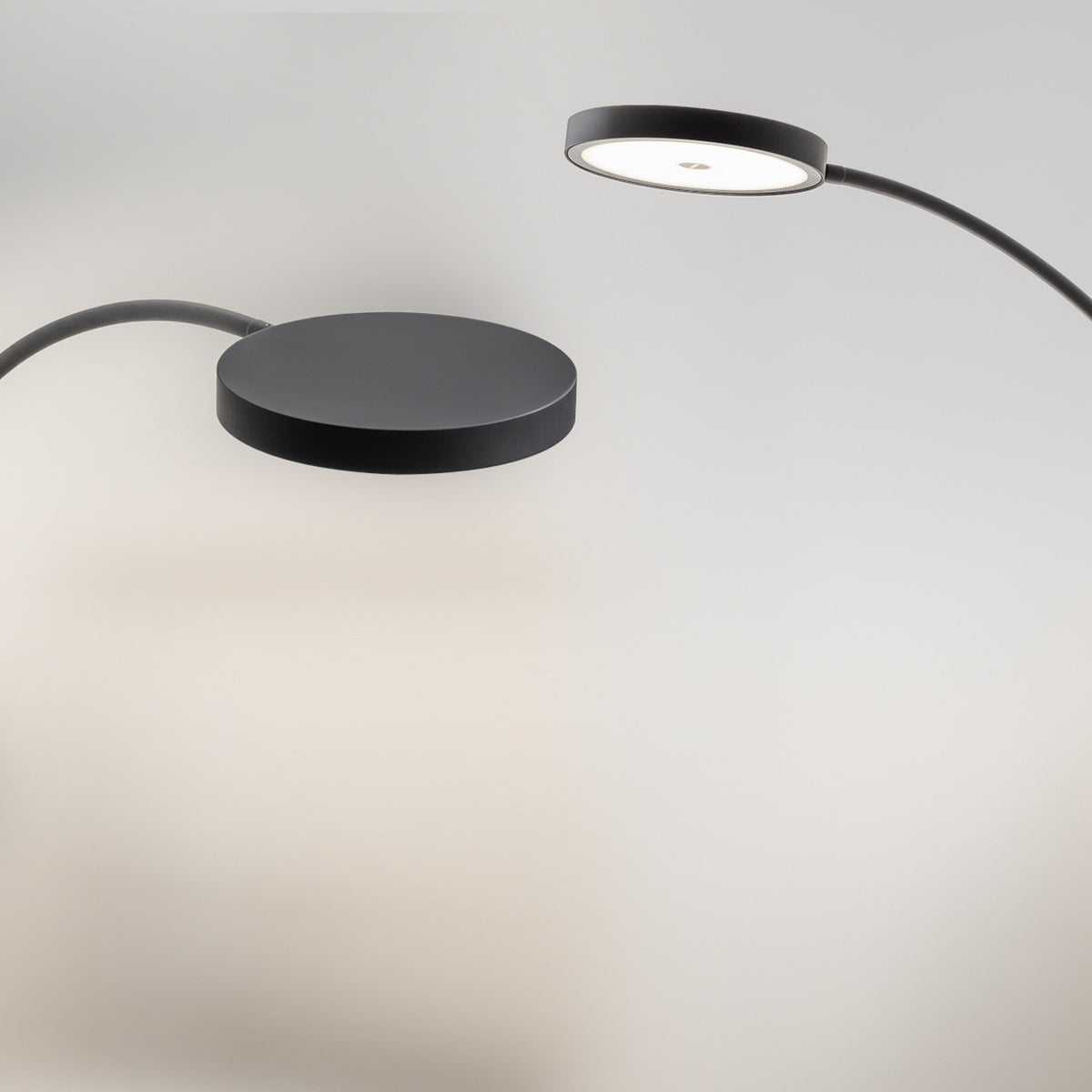 Dip Nero Marquina arc LED floor lamp with a slim curved arm, round matt black base and flat round head showing the integrated warm white LED, shown against a plain light grey background.