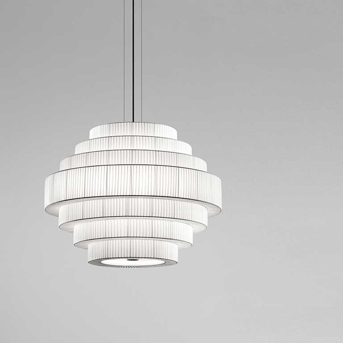 Mos 03 Ribbon Tiered Pendant Light with stacked white pleated ribbon rings forming a rounded tower shade, suspended on thin cables against a plain grey background.
