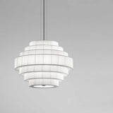 Mos 03 Ribbon Tiered Pendant Light with stacked white pleated ribbon rings forming a rounded tower shade, suspended on thin cables against a plain grey background.
