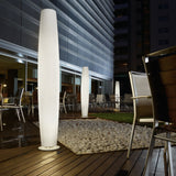 Maxi P/180 tall white polyethylene outdoor floor lamp with ribbed cylindrical shade and round base, illuminated on a restaurant terrace at night alongside a matching smaller model.