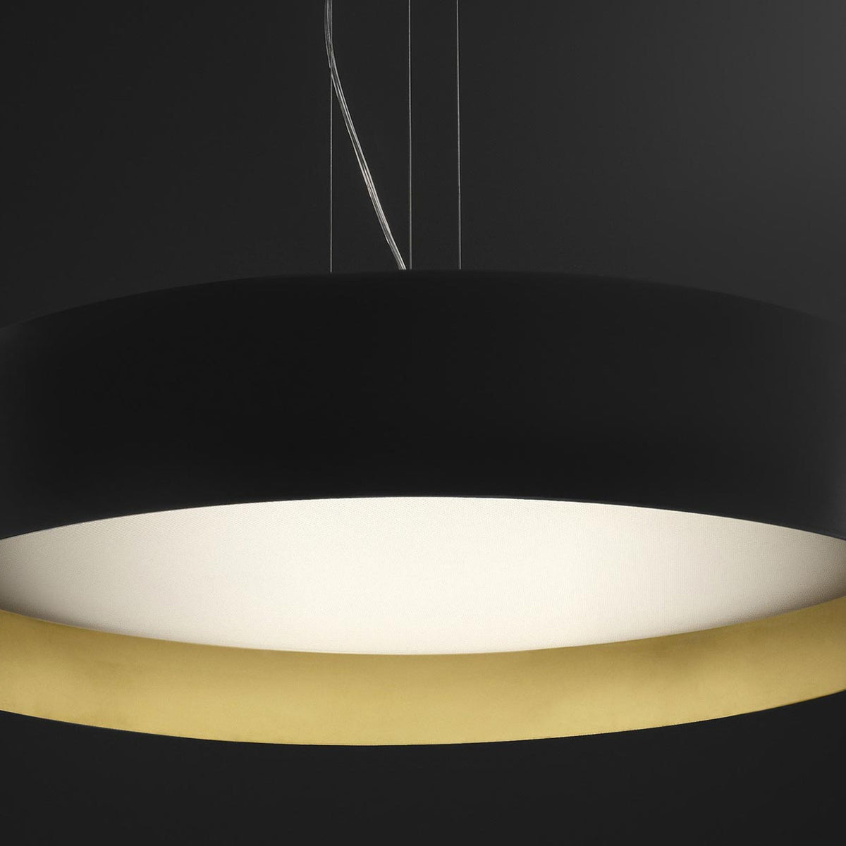 Close-up of the Ginevra 80cm LED pendant light, a wide matt black drum with a brass inner rim framing a white diffuser, shown against a dark background.