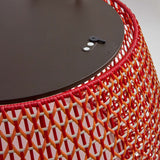 Close-up of the Nans Bag/38/R outdoor floor lamp showing its woven red and orange lattice shade and flat dark top with a teak lifting handle.