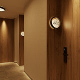 Ring W1 Number Glass Ring wall light in dark wood finish, round fitting with illuminated white disc showing room number "410," mounted on wood-panelled hotel corridor wall.