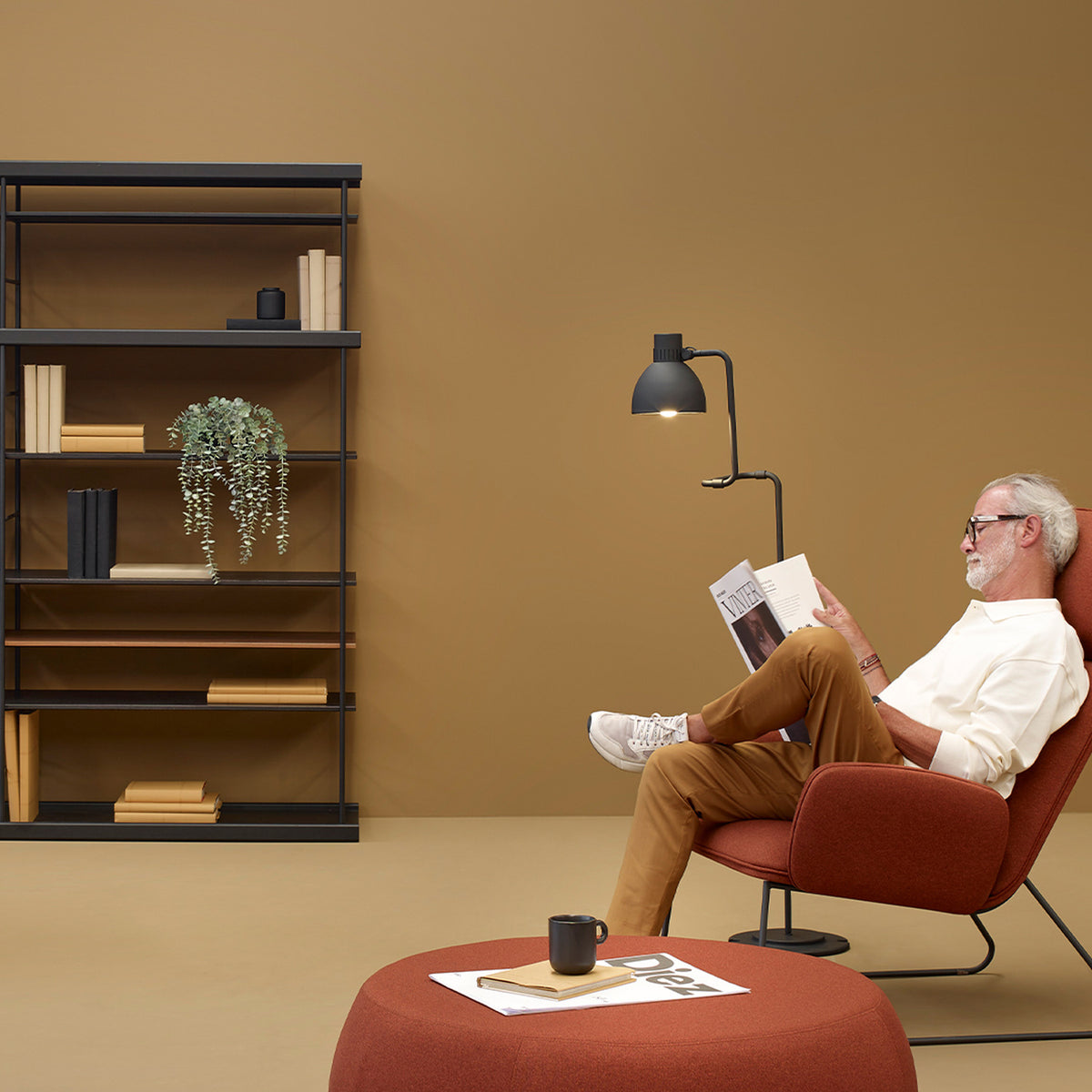 Blux F30 Aluminium Dome Floor Lamp in matte black with a jointed arm and round base, shown beside an armchair in a warm-toned living room.