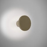 Arid A/01 round aluminium LED wall light with vertically fluted disc in Textured Olive Grey, mounted on a short stem casting a soft halo glow on a plain light background.