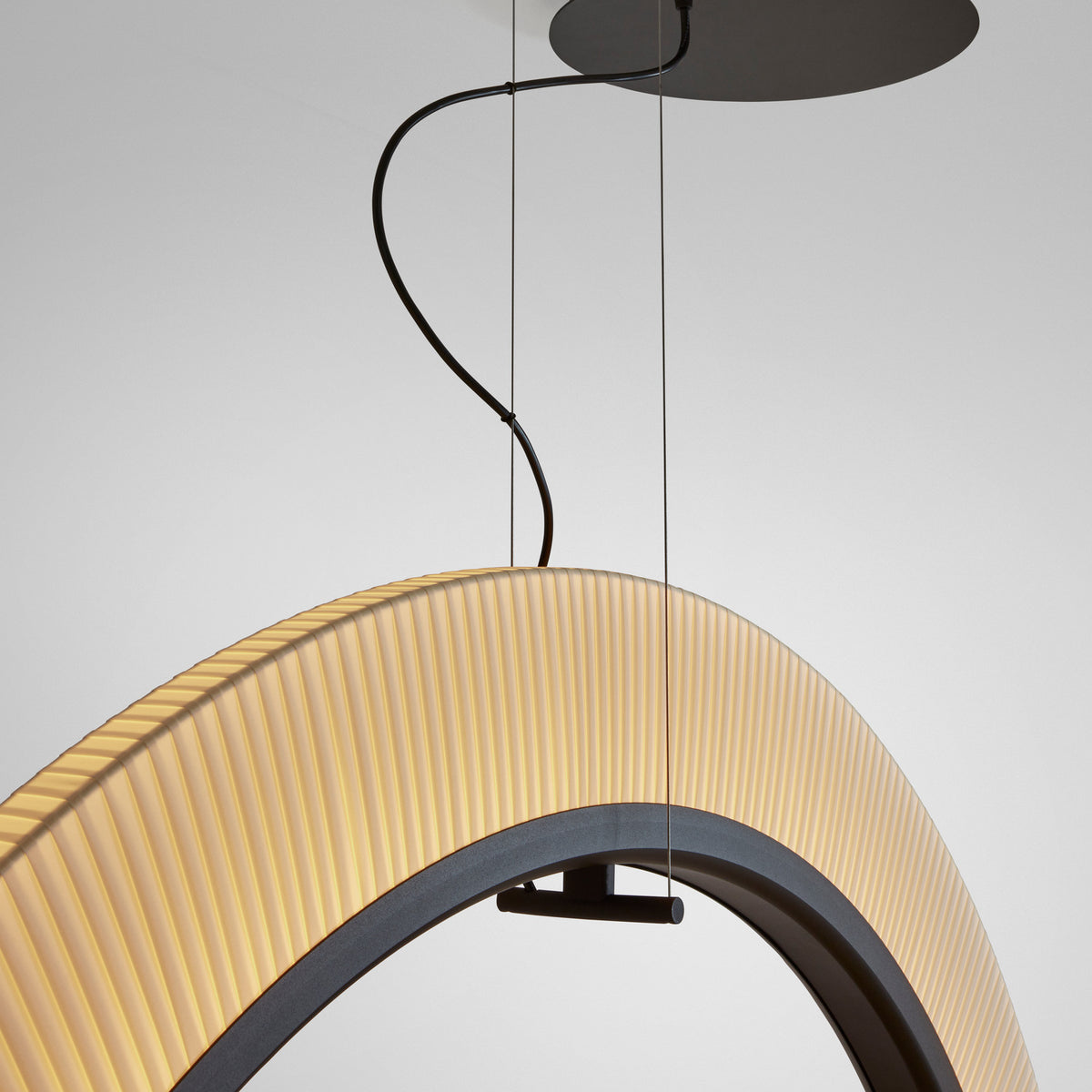 Roda S/120 Ribbon Ring LED pendant light, close-up of pleated white translucent ring shade with dark inner band and black ceiling mount cables on a plain grey background.