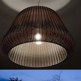 Ralph woven outdoor pendant light, 90cm bell-shaped shade in metallic brown, glowing E27 bulb visible through the open weave, shown outdoors at dusk.