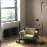 Speers F 2 Light LED Floor Lamp in matte black, two slim stems with small dome heads at different heights on a round base, shown beside an armchair in a living room.