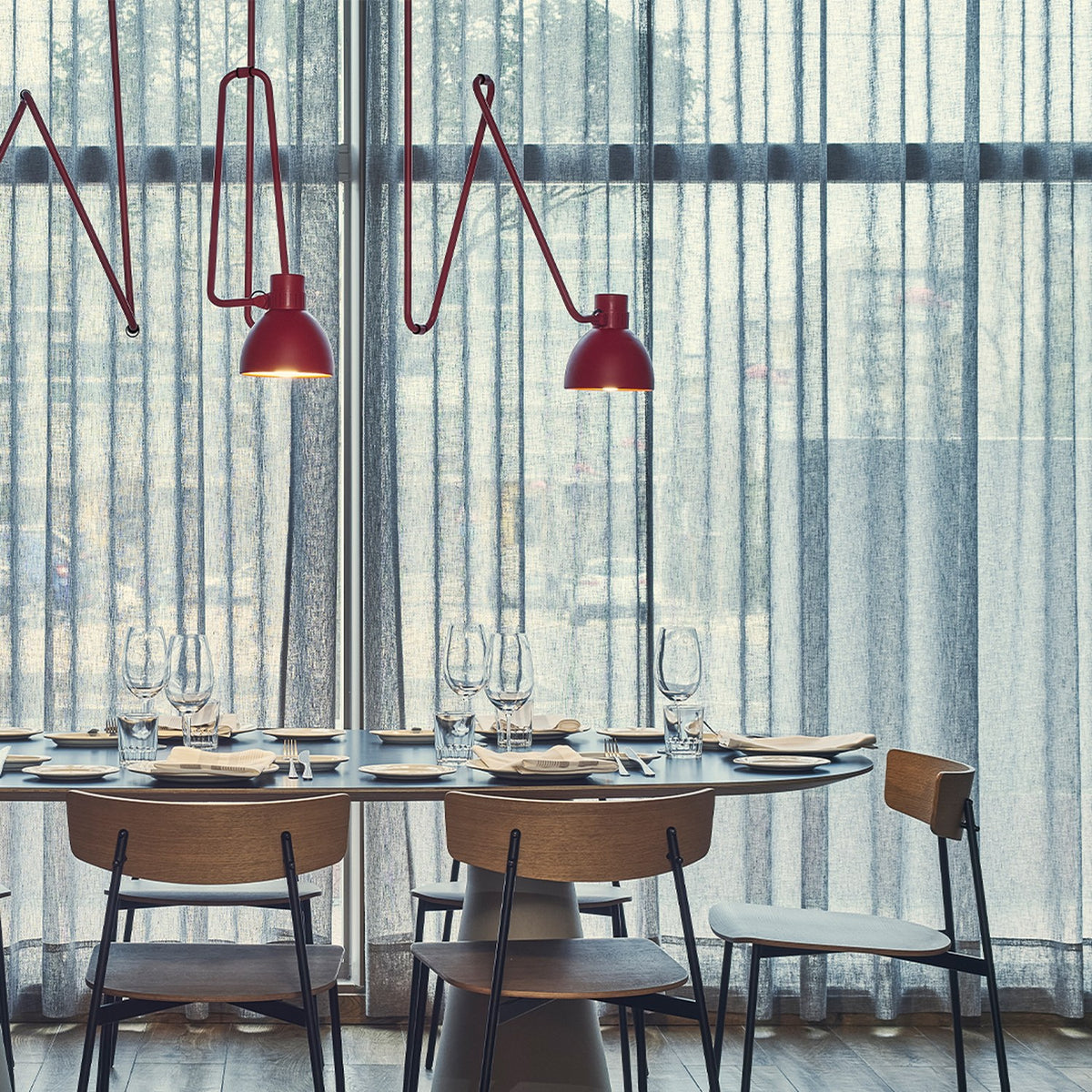 Blux C Aluminium Dome Ceiling Light in red, shown in a dining setting with zig-zag arms and dome shades above a table with wooden chairs and sheer curtains.
