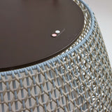 Close-up of the Nans Bag/38 Wood LED outdoor floor lamp showing its dark round top and woven open-weave shade in beige, with crossing wicker-style strands against a plain light background.
