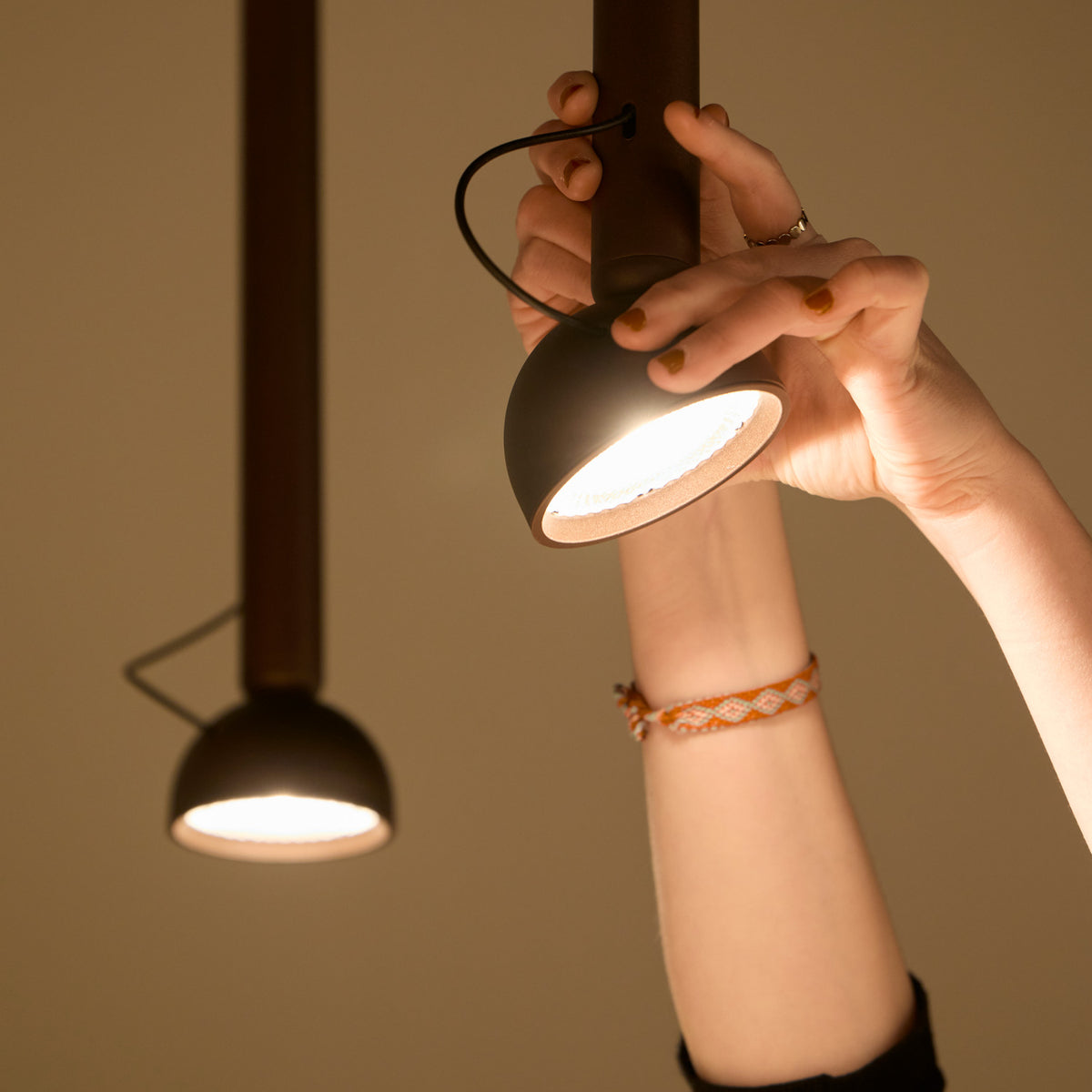 Berry S Aluminium LED pendant light in matte black with a slim tube and angled domed head, shown lit as a hand adjusts its direction.