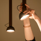 Berry S Aluminium LED pendant light in matte black with a slim tube and angled domed head, shown lit as a hand adjusts its direction.