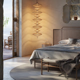 Yuyun S/7C Fabric LED Pendant Light in Satin Beige, a tall column of seven woven round tiers on a single stem, shown glowing warmly beside a bed in a coastal-style bedroom.