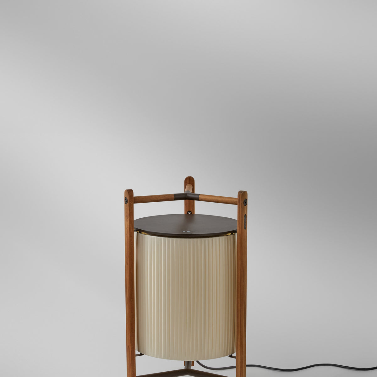 Kando P/76 floor lamp with a pleated cream translucent ribbon cylinder shade, teak wood tripod frame, and round dark brown top, shown on a plain light background.