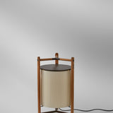 Kando P/76 floor lamp with a pleated cream translucent ribbon cylinder shade, teak wood tripod frame, and round dark brown top, shown on a plain light background.