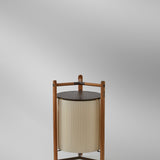 Kando P/76/R rechargeable LED floor lamp with pleated white ribbon shade in a brown wood and aluminium tripod frame, topped with a flat round disc, on a plain grey background.