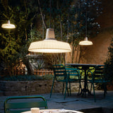 Marietta S/32 Dome LED Outdoor Pendant Light in white, with a pleated dome shade on a black cable, shown illuminated above a garden dining table at night.