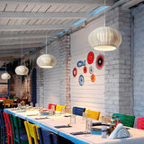 Garota S/02 globe pendant lights in Ivory White woven shade finish, hung at varying heights above a long dining table in a coastal-style restaurant setting.