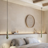 Two Slend 02 aluminium pendant lights in sage green with slim tapering bodies and ringed lower sections, hung above a bedroom shelf and bed.