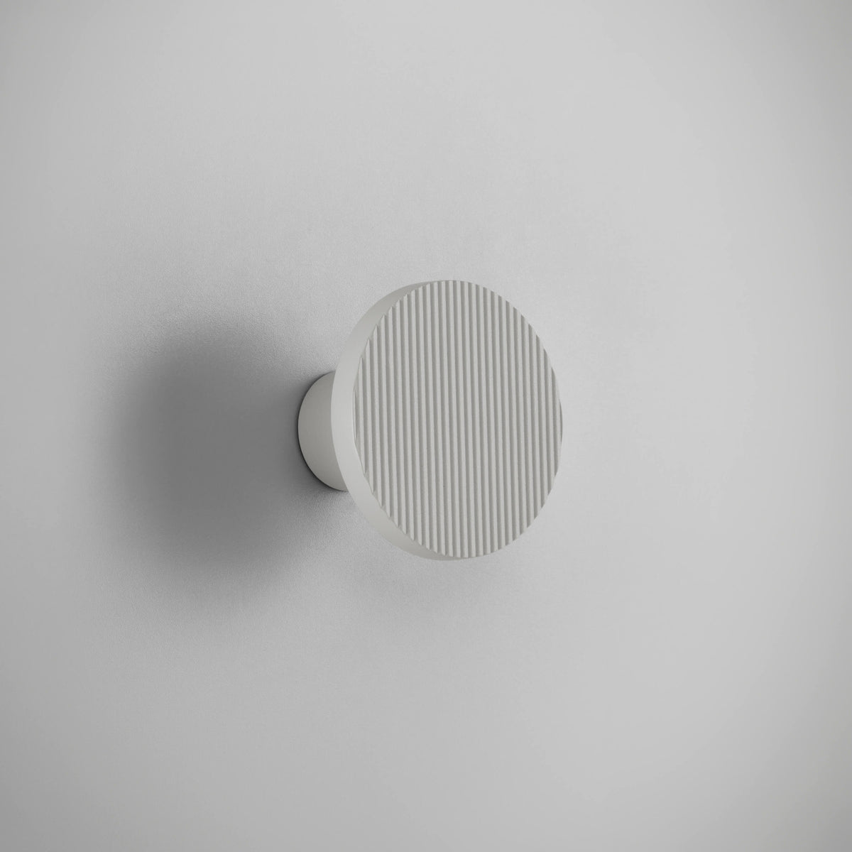 Arid A/01 round LED wall light in textured white aluminium, flat fluted disc on a short stem, mounted on a plain light grey background.